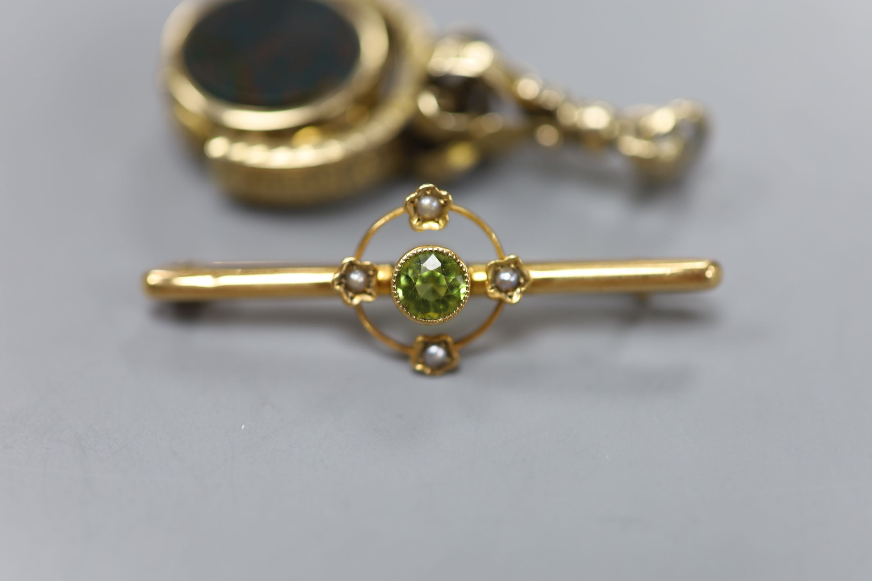 A Victorian yellow metal overlaid, bloodstone and sardonyx set swivelling fob seal, 42mm and a 9ct, peridot and seed pearl set bar brooch, 40mm.